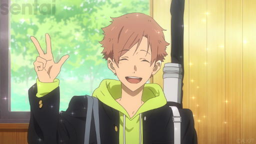 Tsurune’s Nanao, a good-looking boy with light brown hair, holds up his hand in a victory V. He wears a green shirt under a black school uniform jacket; sparkles float around him, complementing his warm and friendly grin.
