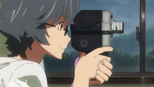 A smiling Kaito Kirishima from Waiting in the Summer peers into the viewfinder of an old-fashioned camera.