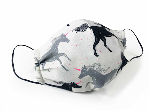 A white face mask patterned with black and grey unicorns with pink horns, courtesy of The Raspberry Room, sits on a white background.