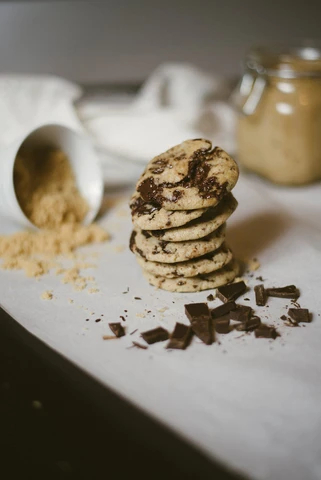 Delicious chocolate chip cookies from Tubby's Taste sit on a white table in front of baking ingredients. They look delicious. We want them.